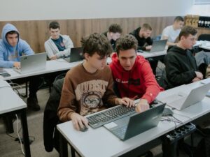 Ученици работят по проекти на лаптопи в модерна учебна зала.